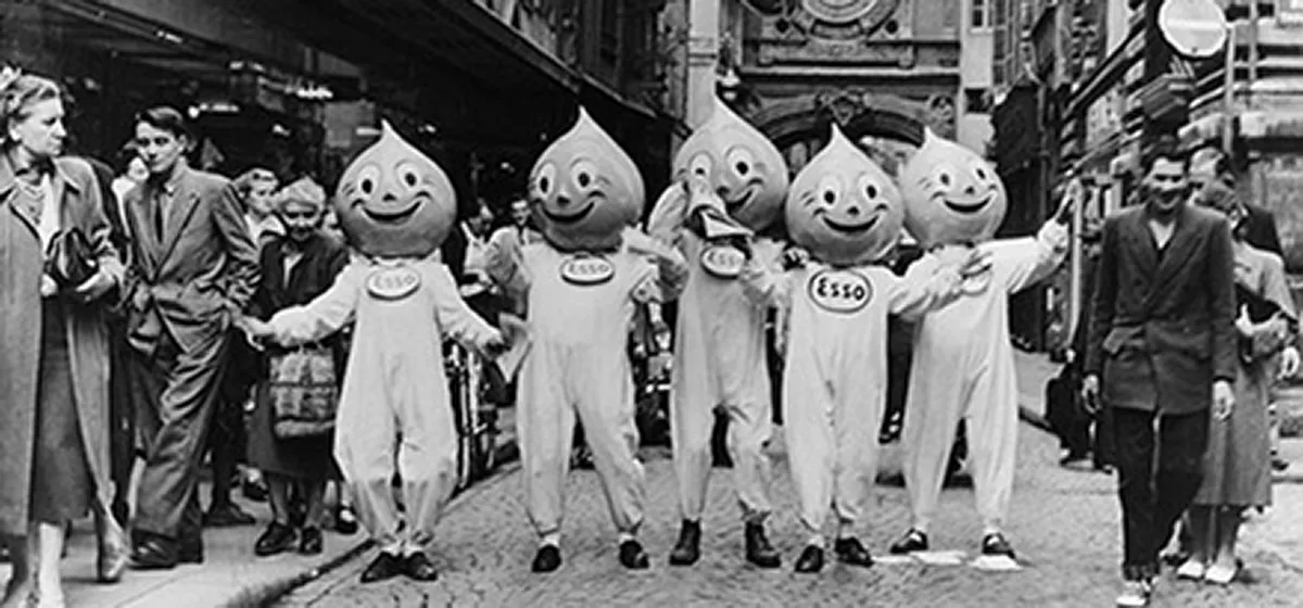 Vintage 1950s black and white photo of five Esso "Happy" the Oil Drop Man mascots promoting the Happy Motoring campaign on a city street.