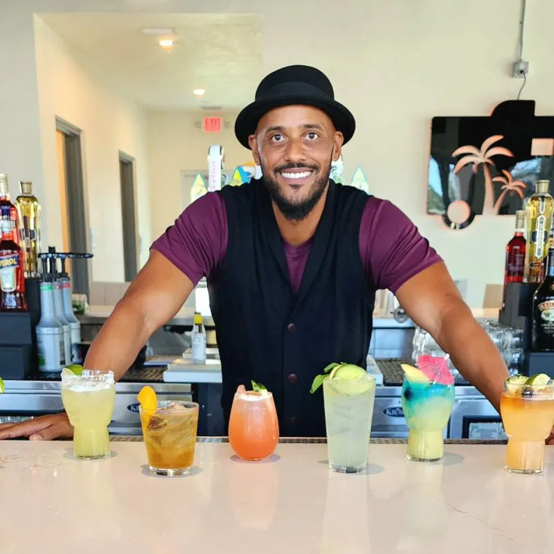 Phil Wills behind a bar with six vibrant craft cocktails. Bar Rescue co-host and beverage consultant demonstrating menu innovation and the Art of Hospitality.