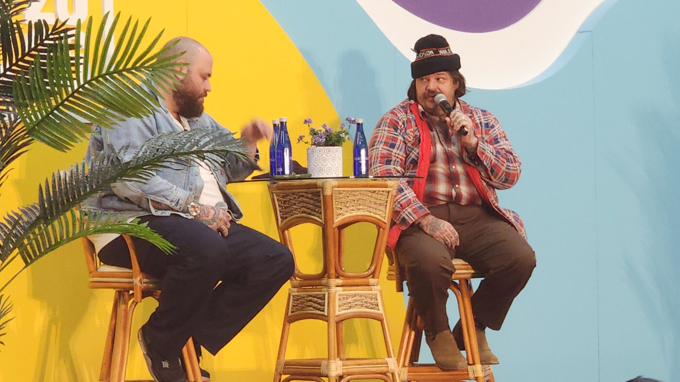 Christian Petroni and Matty Matheson on stage at Baldor BITE 2026, seated in wicker chairs during their live interview for 86'd Me magazine.