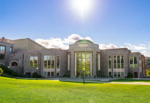 Exterior view of the Marist University campus building featuring stone architecture, large glass windows, and a green lawn under a sunny sky in Poughkeepsie, New York