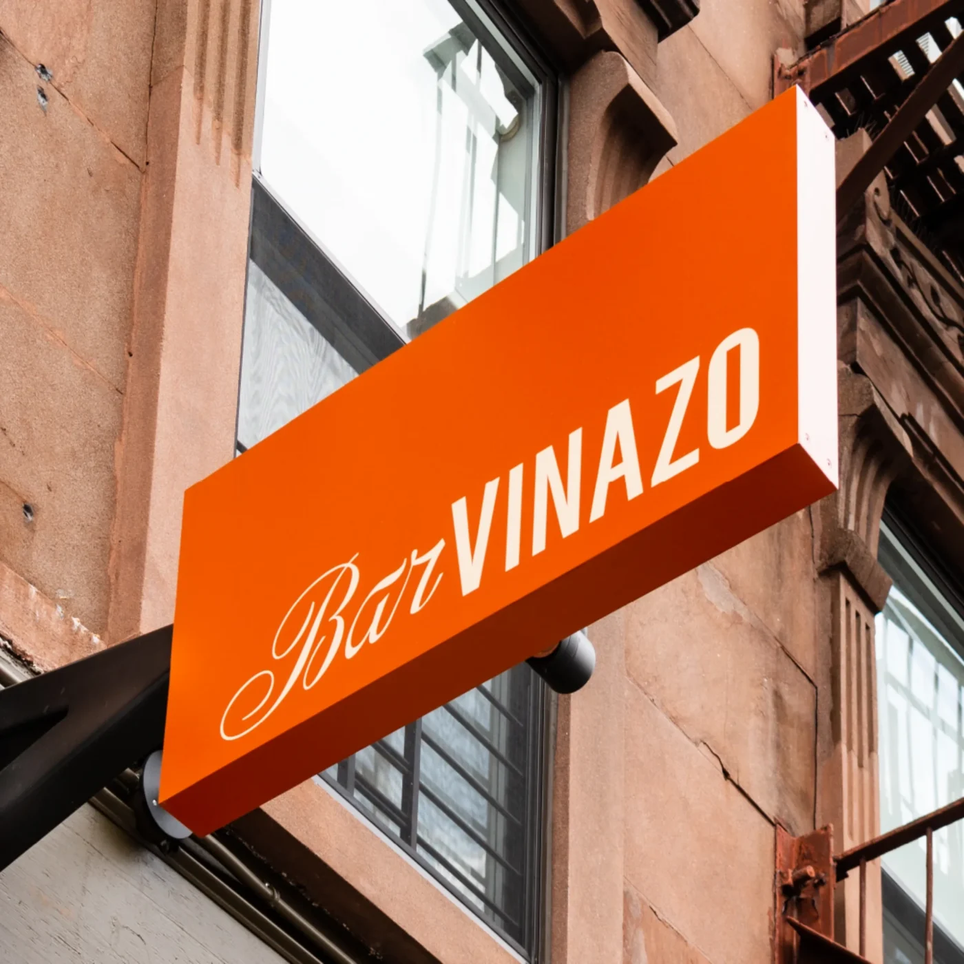 Orange exterior sign for Bar Vinazo mounted on a brownstone building facade.
